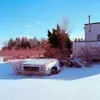 Photo of snowy scene with a dilapidated car in the foreground and crumbling building in background