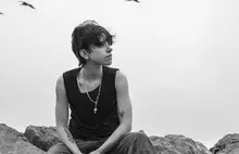 Maria BC wears a black tank top and sits on top of grey boulders.