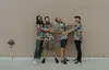 The four members of Atomicos are hugging while standing in front of a beige brick wall. The bass player does not appear to be enjoying himself.  