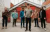 The six members of Starpainter stand in a dilapidated alley. Lead singer/songwriter Joel Stretch stands a little ahead of the others.